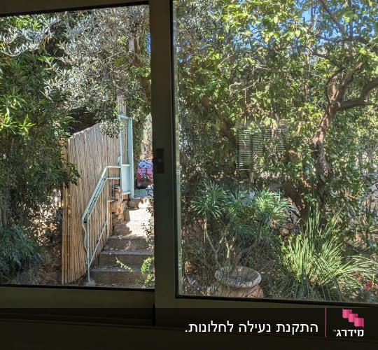 תריסים סגורים על חלון זכוכית עם נוף גינה ירוקה
